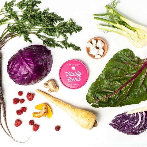 Vitality Blend container surrounded by fresh vegetables and fruits on a white background